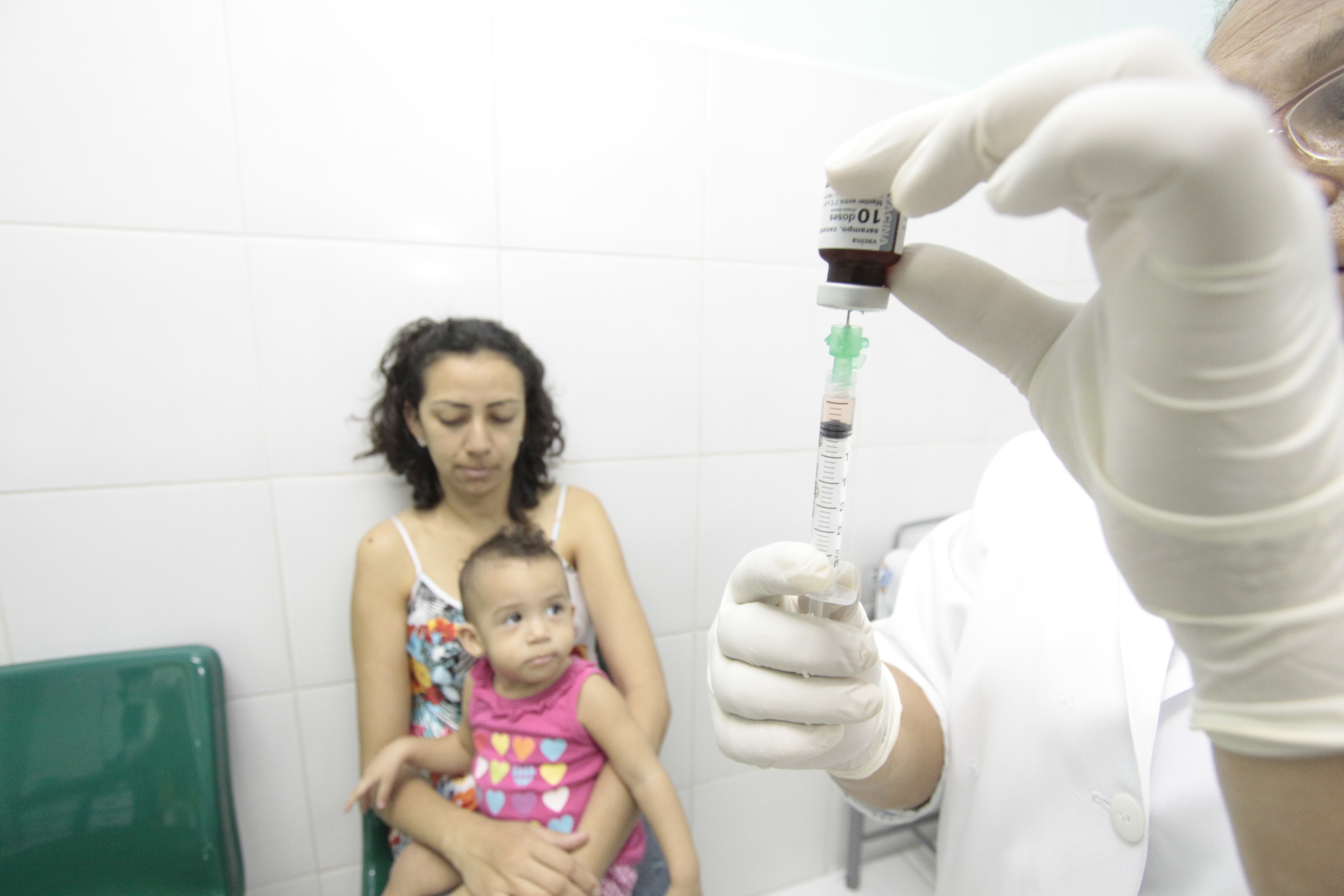 Mulher com criança no colo ao lado de enfermeira preparando vacina